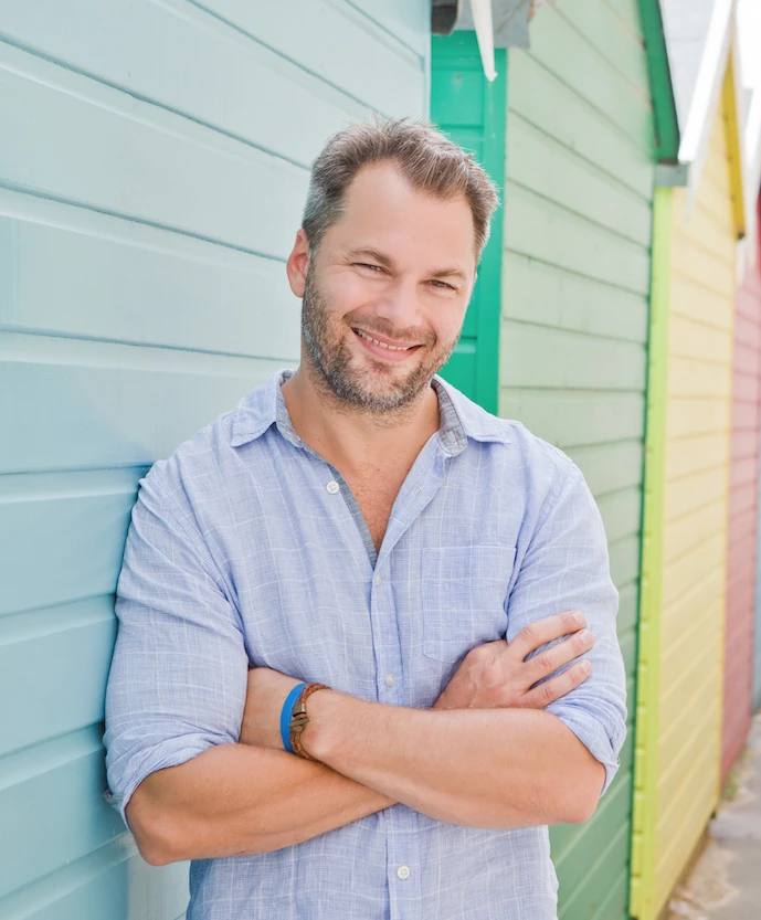 Chris Finn smiling beside colourful beach huts